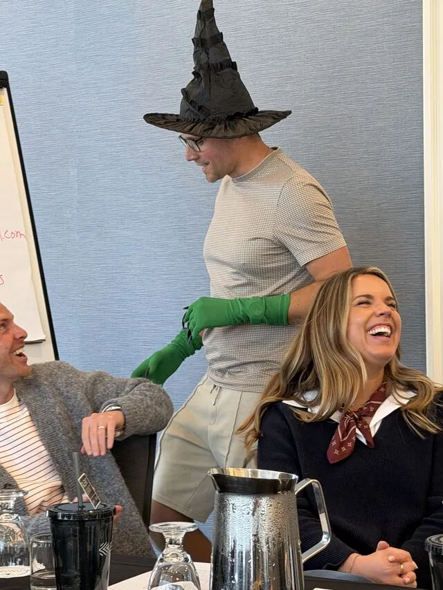 A colleague in a witch hat and green gloves getting a laugh at the front of the room